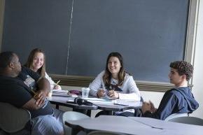 Four students study together around a table in front of a chalkboard