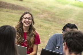 A small group of students sits outdoors with laptops while working together