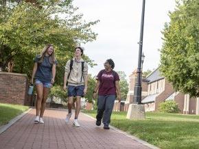 Three students walking across campus with Grace Chapel 和 Shaw Plaza in the background