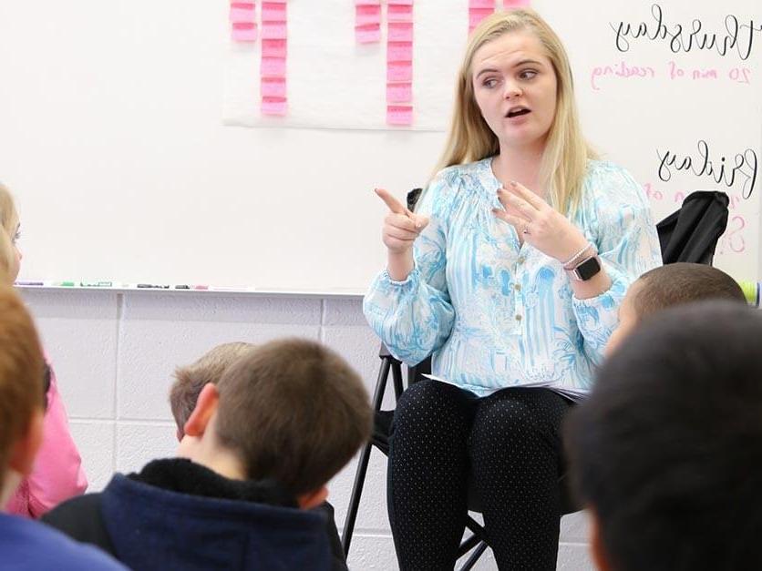 A student teacher interacts with elementary kids in front of the classroom.