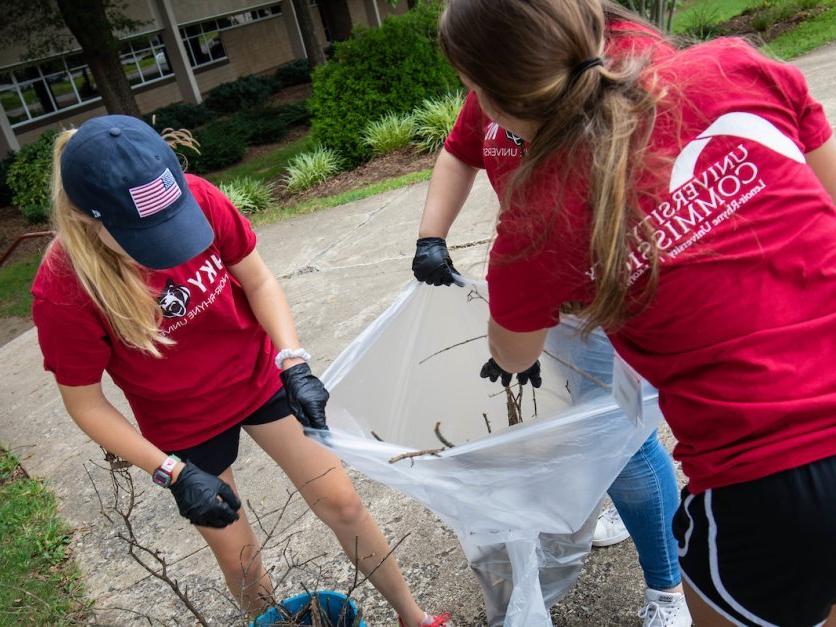 Three student volunteers clean up yard debris as part of a community service project.